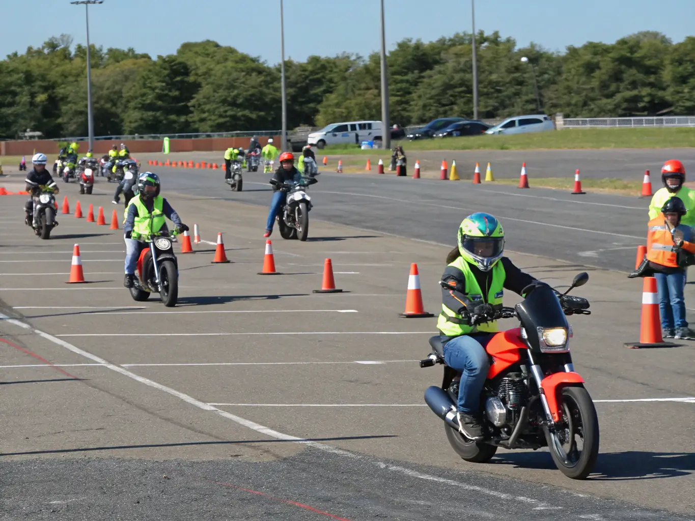 A group of young people participating in a motorcycle initiation program, wearing safety gear and being supervised by instructors on a closed, safe course.